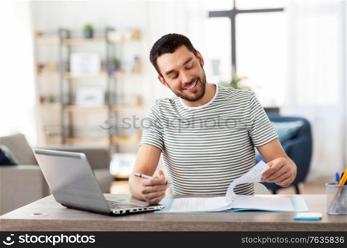 remote job and business concept - happy smiling man with papers and laptop computer working at home office. man with papers and laptop working at home office
