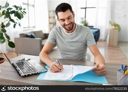 remote job and business concept - happy smiling man with papers and laptop computer working at home office. man with papers and laptop working at home office