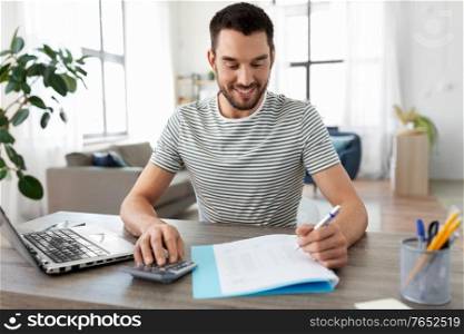 remote job and business concept - happy smiling man with papers, calculator and laptop computer working at home office. man with files and calculator works at home office