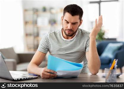 remote job and business concept - stressed man with papers and laptop computer working at home office. man with papers and laptop working at home office