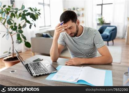 remote job and business concept - stressed man with papers and laptop computer working at home office. man with papers and laptop working at home office