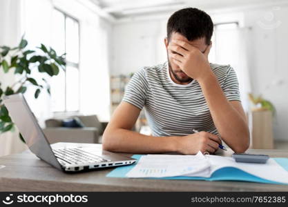 remote job and business concept - stressed man with papers and laptop computer working at home office. man with papers and laptop working at home office