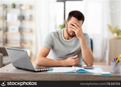 remote job and business concept - stressed man with papers, calculator and laptop computer working at home office. man with files and calculator works at home office