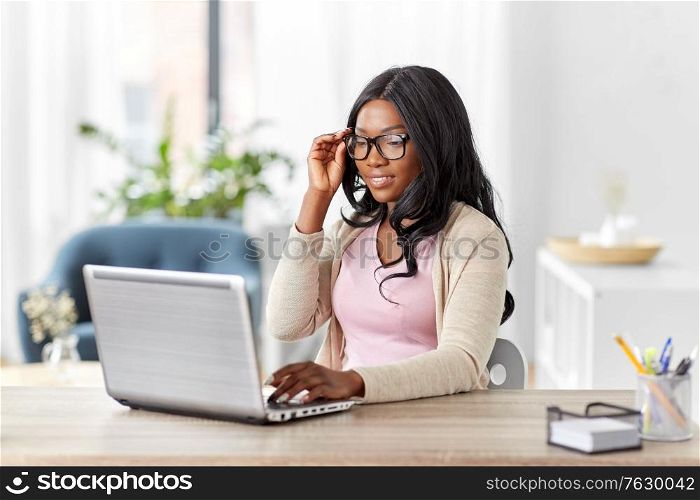 remote job, business and e-learning concept - happy smiling young african american woman in glasses with laptop computer working at home office. african woman with laptop working at home office