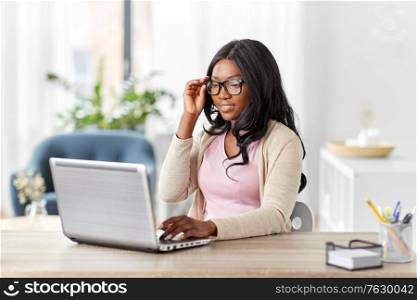 remote job, business and e-learning concept - happy smiling young african american woman in glasses with laptop computer working at home office. african woman with laptop working at home office