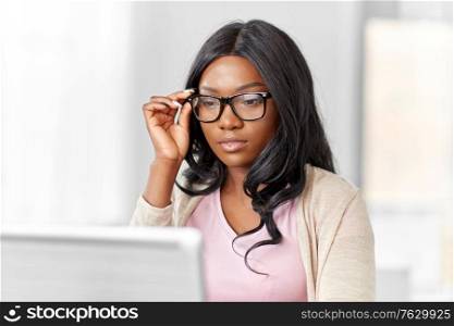 remote job, business and e-learning concept - young african american woman in glasses with laptop computer working at home office. african woman with laptop working at home office