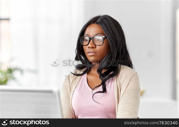 remote job, business and e-learning concept - young african american woman in glasses with laptop computer working at home office. african woman with laptop working at home office
