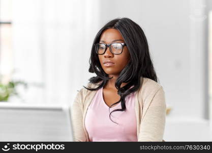 remote job, business and e-learning concept - young african american woman in glasses with laptop computer working at home office. african woman with laptop working at home office