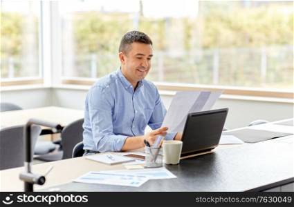 remote job, business and people concept - happy smiling middle-aged man with laptop computer and papers working at home office. man with laptop and papers working at home office