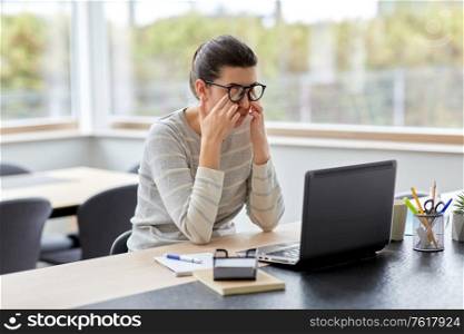 remote job, business and vision concept - tired young woman in glasses with laptop computer working at home office and rubbing her eyes. tired woman with laptop working at home office