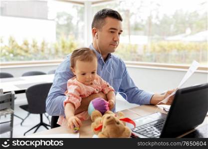 remote job, multi-tasking and family concept - middle-aged father in earphones with baby, laptop and papers working at home office. father with baby and papers working at home office