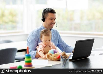 remote job, multi-tasking and family concept - middle-aged father in headset with baby working on laptop at home office. father with baby working on laptop at home office