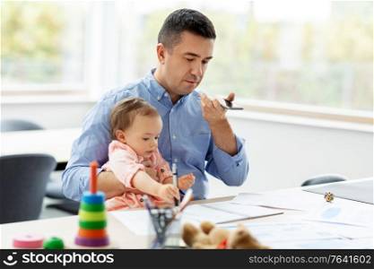 remote job, multi-tasking and family concept - middle-aged father with baby using voice command recorder on smartphone at home office. father with baby and phone working at home office