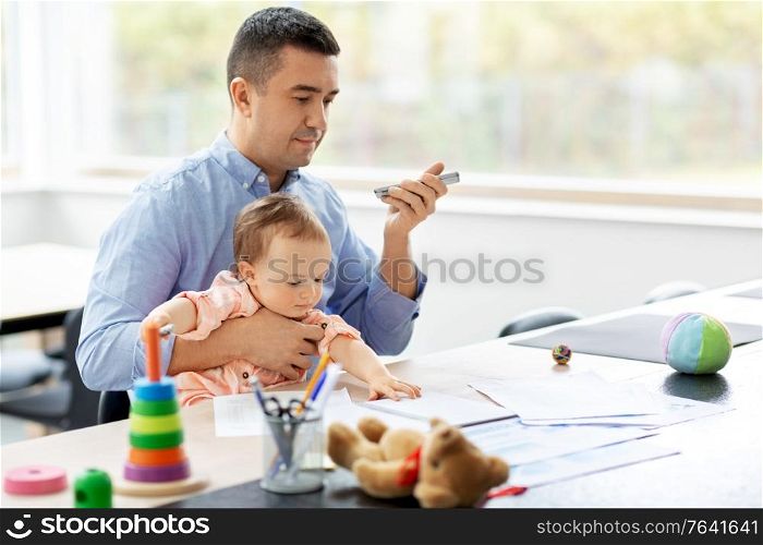 remote job, multi-tasking and family concept - middle-aged father with baby using voice command recorder on smartphone at home office. father with baby and phone working at home office