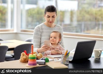 remote job, multi-tasking and family concept - mother with baby, smartphone and laptop working at home office. mother with baby and phone working at home office