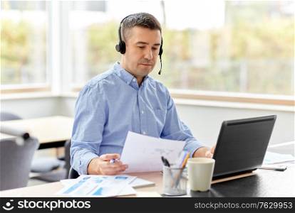remote job, technology and business concept - middle-aged man with headset and laptop computer having conference call at home office. man with headset and laptop working at home