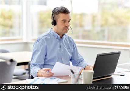 remote job, technology and business concept - middle-aged man with headset and laptop computer having conference call at home office. man with headset and laptop working at home