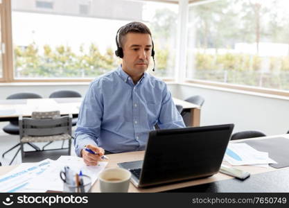 remote job, technology and business concept - middle-aged man with headset and laptop computer having conference call at home office. man with headset and laptop working at home