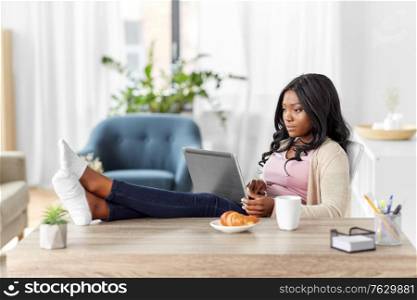 remote job, technology and people concept - african american young woman with laptop computer working at home office and resting her feet on table. african woman with laptop working at home office