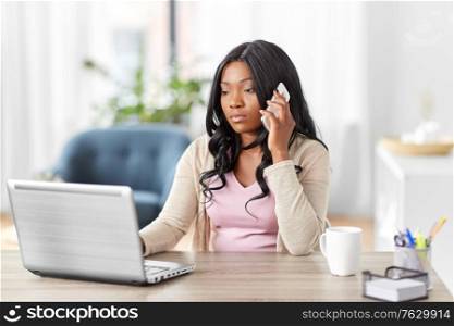 remote job, technology and people concept - african american young woman with laptop computer working at home office and calling on smartphone. woman with laptop calling on phone at home office