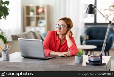 remote job, technology and people concept - bored or tired young woman in glasses with laptop computer working at home office. bored woman with laptop working at home office