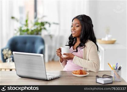 remote job, technology and people concept - happy smiling african american young woman with laptop computer drinking coffee at home office. happy woman with laptop and coffee at home office