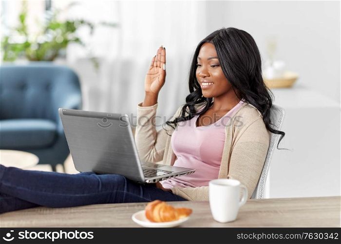 remote job, technology and people concept - happy smiling african american young woman with laptop computer having video call at home office and resting her feet on table. happy woman with laptop working at home office