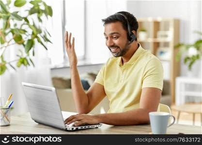 remote job, technology and people concept - happy smiling indian man with headset and laptop computer having conference call at home office. indian man with headset and laptop working at home