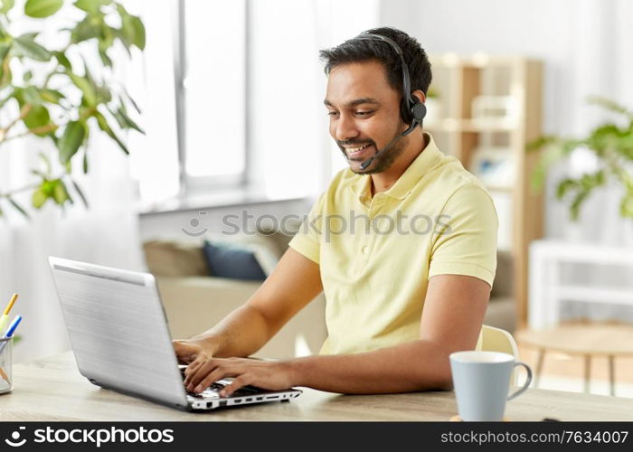 remote job, technology and people concept - happy smiling indian man with headset and laptop computer having conference call at home office. indian man with headset and laptop working at home