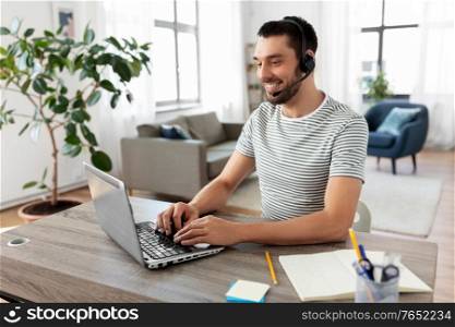remote job, technology and people concept - happy smiling man with headset and laptop computer having video conference at home office. man with headset and laptop working at home