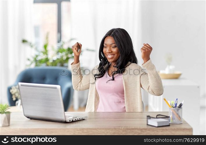 remote job, technology and people concept - happy smiling young african american woman with laptop computer working at home office and celebrating success. happy woman with laptop working at home office