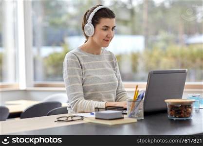 remote job, technology and people concept - happy smiling young woman in headphones with laptop computer working at home office. woman in headphones with laptop working at home