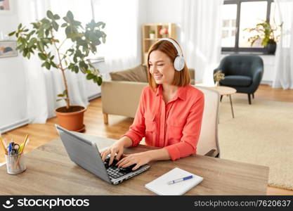 remote job, technology and people concept - happy smiling young woman in headphones with laptop computer working at home office. woman in headphones with laptop working at home