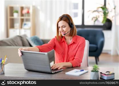 remote job, technology and people concept - happy smiling young woman with headset and laptop computer having video conference at home office. woman with headset and laptop working at home