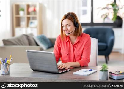 remote job, technology and people concept - happy smiling young woman with headset and laptop computer having video conference at home office. woman with headset and laptop working at home