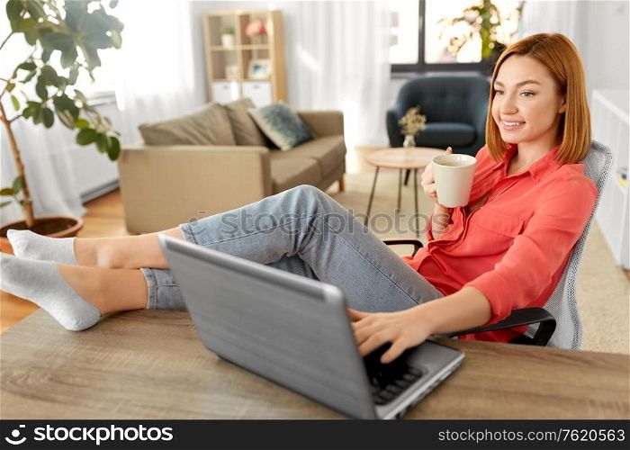 remote job, technology and people concept - happy smiling young woman with laptop computer drinking coffee at home office and resting her feet on table. woman with laptop drinking coffee at home office