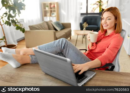 remote job, technology and people concept - happy smiling young woman with laptop computer drinking coffee at home office and resting her feet on table. woman with laptop drinking coffee at home office