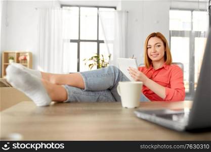 remote job, technology and people concept - happy smiling young woman with notebook and laptop computer at home office resting feet on table. woman with notebook and laptop at home office