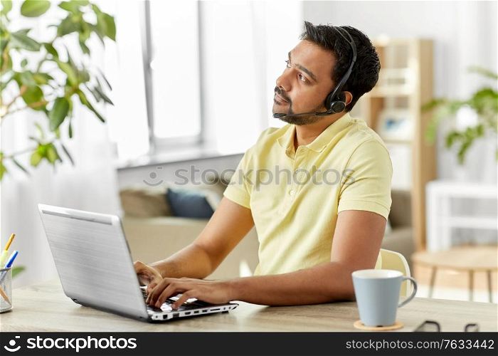 remote job, technology and people concept - indian man with headset and laptop computer thinking at home office. indian man with headset and laptop working at home