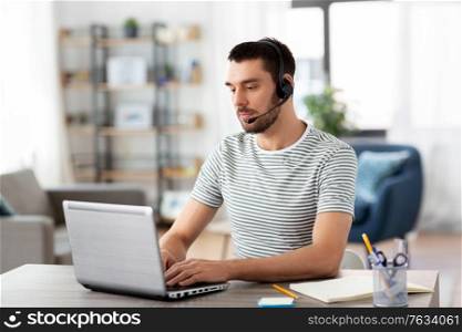 remote job, technology and people concept - man with headset and laptop computer having video conference at home office. man with headset and laptop working at home