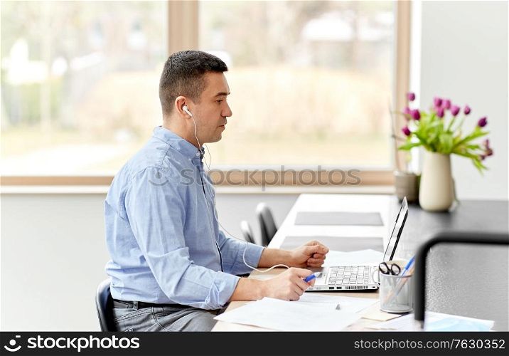 remote job, technology and people concept - middle-aged man in earphones with laptop computer and papers working at home office and having video call. man in earphones with laptop working at home