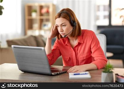 remote job, technology and people concept - sad young woman with headset and laptop computer having video conference at home office. sad woman with headset and laptop working at home