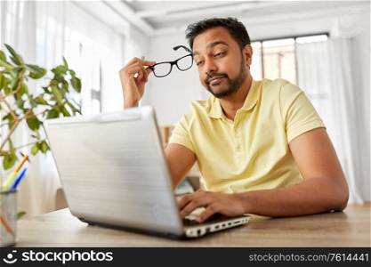 remote job, technology and people concept - stressed young indian man with glasses and laptop computer working at home office. stressed man with laptop working at home office