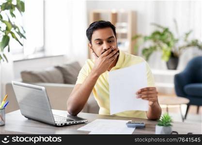 remote job, technology and people concept - stressed young indian man with calculator and papers working at home office. man with calculator and papers working at home