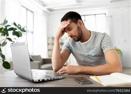 remote job, technology and people concept - stressed young man with laptop computer having headache at home office. stressed man with laptop working at home office