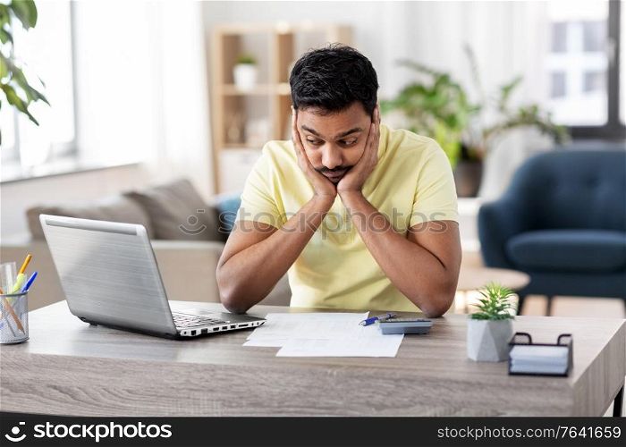 remote job, technology and people concept - unhappy young indian man with calculator and papers working at home office. man with calculator and papers working at home