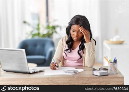 remote job, technology and people concept - young african american woman with calculator and papers working at home office. woman with calculator and papers working at home