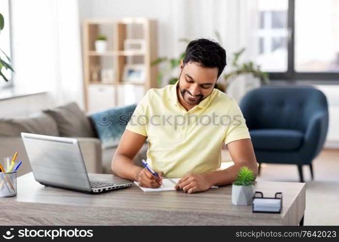remote job, technology and people concept - young indian man with notebook and laptop computer at home office. indian man with notebook and laptop at home office
