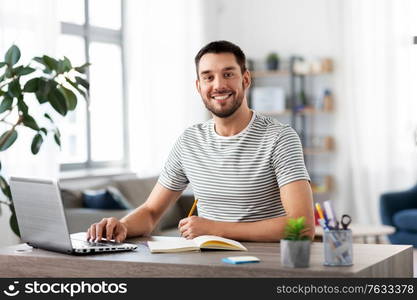 remote job, technology and people concept - young man with notebook and laptop computer working at home office. man with notebook and laptop at home office