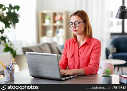 remote job, technology and people concept - young woman in glasses with laptop computer working at home office. woman with laptop working at home office